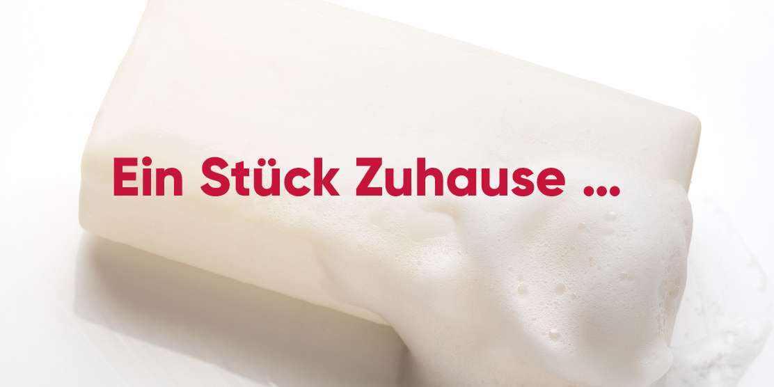 Seife mit Schaum und rotem Text "Ein Stück Zuhause ..."